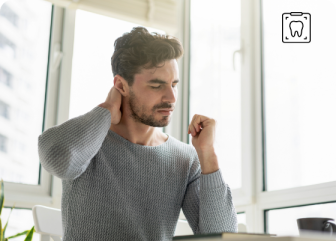 Mann sitzt am Arbeitsplatz und hält sich mit schmerzverzerrtem Gesicht den Nacken. Mann sitzt am Arbeitsplatz und hält sich mit schmerzverzerrtem Gesicht den Nacken.